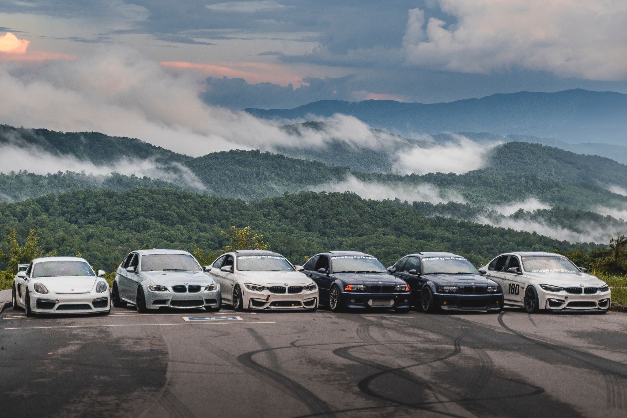 Six cars from the NTBC crew lined up at a mountain overlook with clouds rolling through the valleys